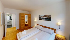 A bedroom with a bed, wooden wardrobe, a bathroom visible through an open door, and a painting on the wall. - Kitzview Idyll Apartment (Zell am See)