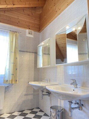 Bathroom features two sinks with modern faucets and a mirror above, set against a tiled backdrop.