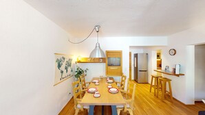 A compact kitchen with a dining area, wooden furniture, a hanging light fixture, and a world map on the wall.