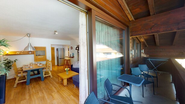 A cozy kitchen with wooden cabinets, a dining table, and a refrigerator. There is a balcony with outdoor seating.