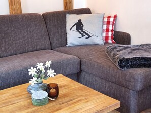 A grey sofa with a silhouette pillow, a small table with a candle, and a vase with flowers.