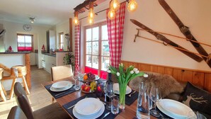 A dining area with a wooden table set for a meal, a ski rack on the wall, and a window with red curtains. - Chalet Salzburg (Niedernsill)