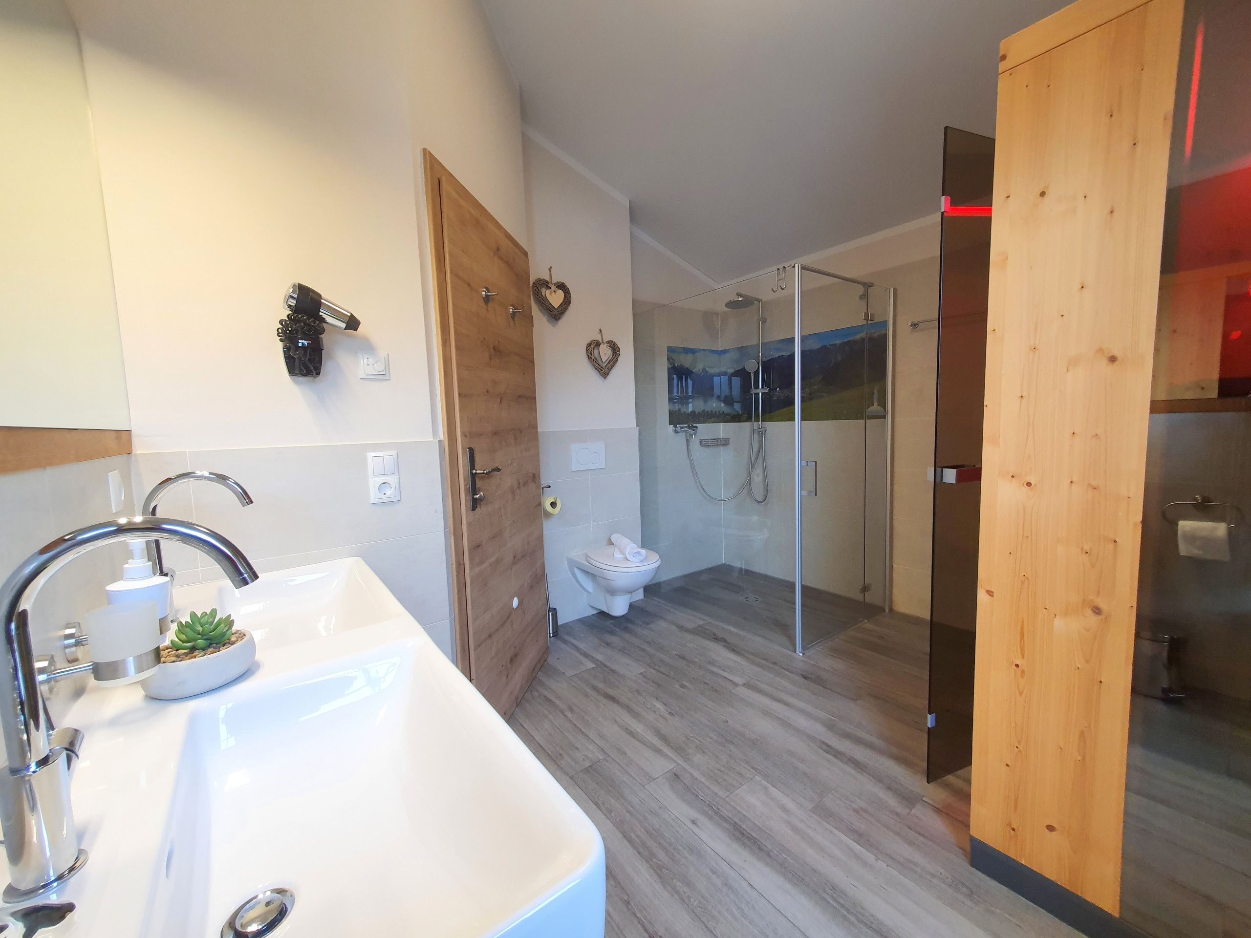 A modern bathroom with a large sink, a shower with glass doors, and wooden accents.