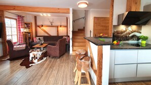 A cozy living room with a fireplace, a dining area, and a kitchen with wooden accents. - Chalet Salzburg (Niedernsill)