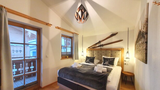A bedroom with a large bed, a window with a view, a hanging light fixture, and a wooden headboard. - Chalet Tauerngold (Niedernsill)