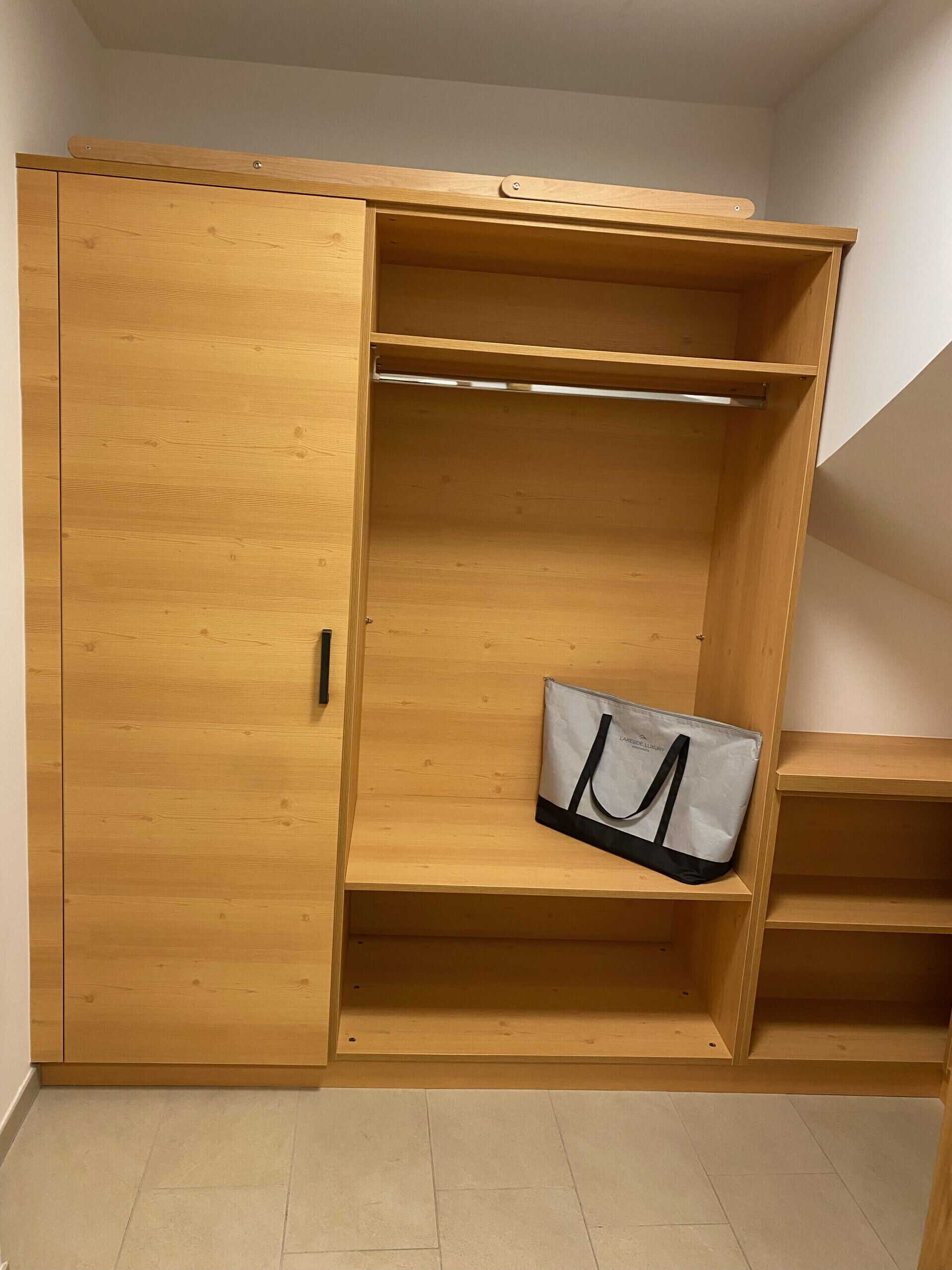 A wooden wardrobe with a sliding door, a hanging bag, and a small shelf.