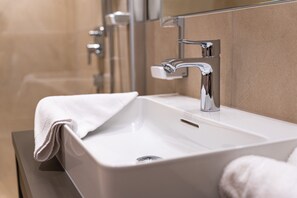 A modern bathroom with a white sink, chrome faucet, and a towel on the counter.