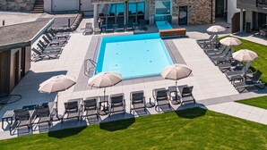 A modern hotel with a swimming pool, outdoor seating, and a view of the surrounding hills. - SPA Apartments Junior Suite 104 (Zell am See)