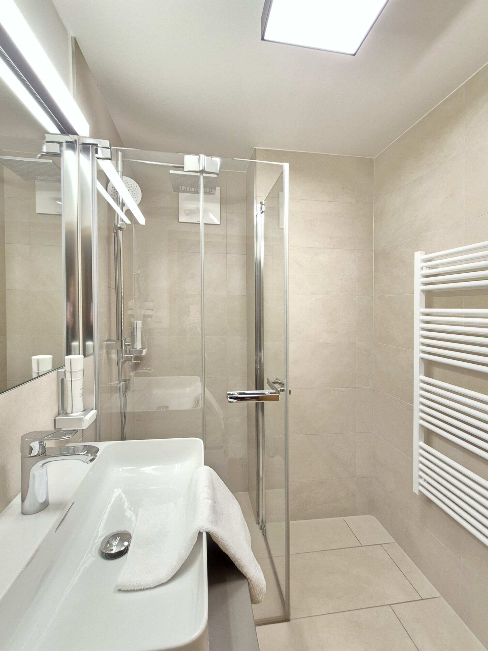 A modern bathroom with a glass shower enclosure, a white sink, and a towel rack.