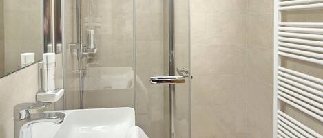 A modern bathroom with a glass shower enclosure, a white sink, and a towel rack.