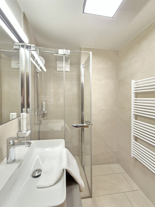A modern bathroom with a glass shower enclosure, a white sink, and a towel rack.