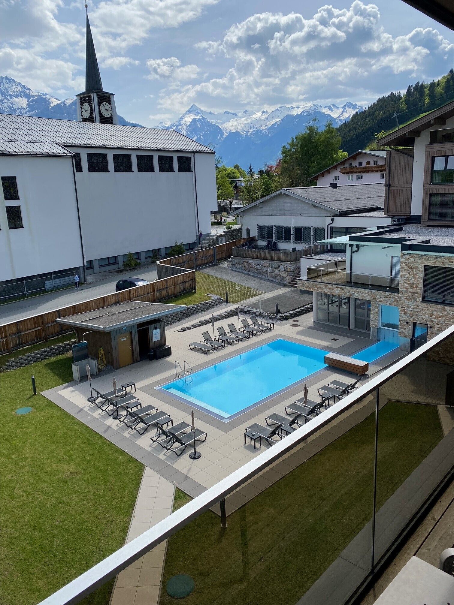 A swimming pool with lounge chairs, a building with a clock tower, and a mountain backdrop.