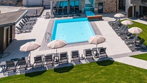Et moderne hotel med swimmingpool, udendørs siddepladser og udsigt til de omkringliggende bakker.