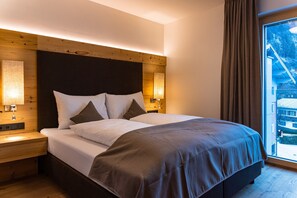 A hotel room with a large bed, wooden headboard, bedside lamps, and a view of a snowy landscape through a window. - SPA Apartments Deluxe Panorama 521 (Zell am See)