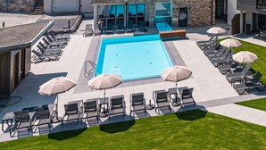 Een modern hotel met een zwembad, terras en uitzicht op de omliggende heuvels.