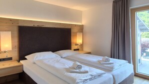 A double bed with white linens, a wooden headboard, bedside lamps, and a window with curtains.