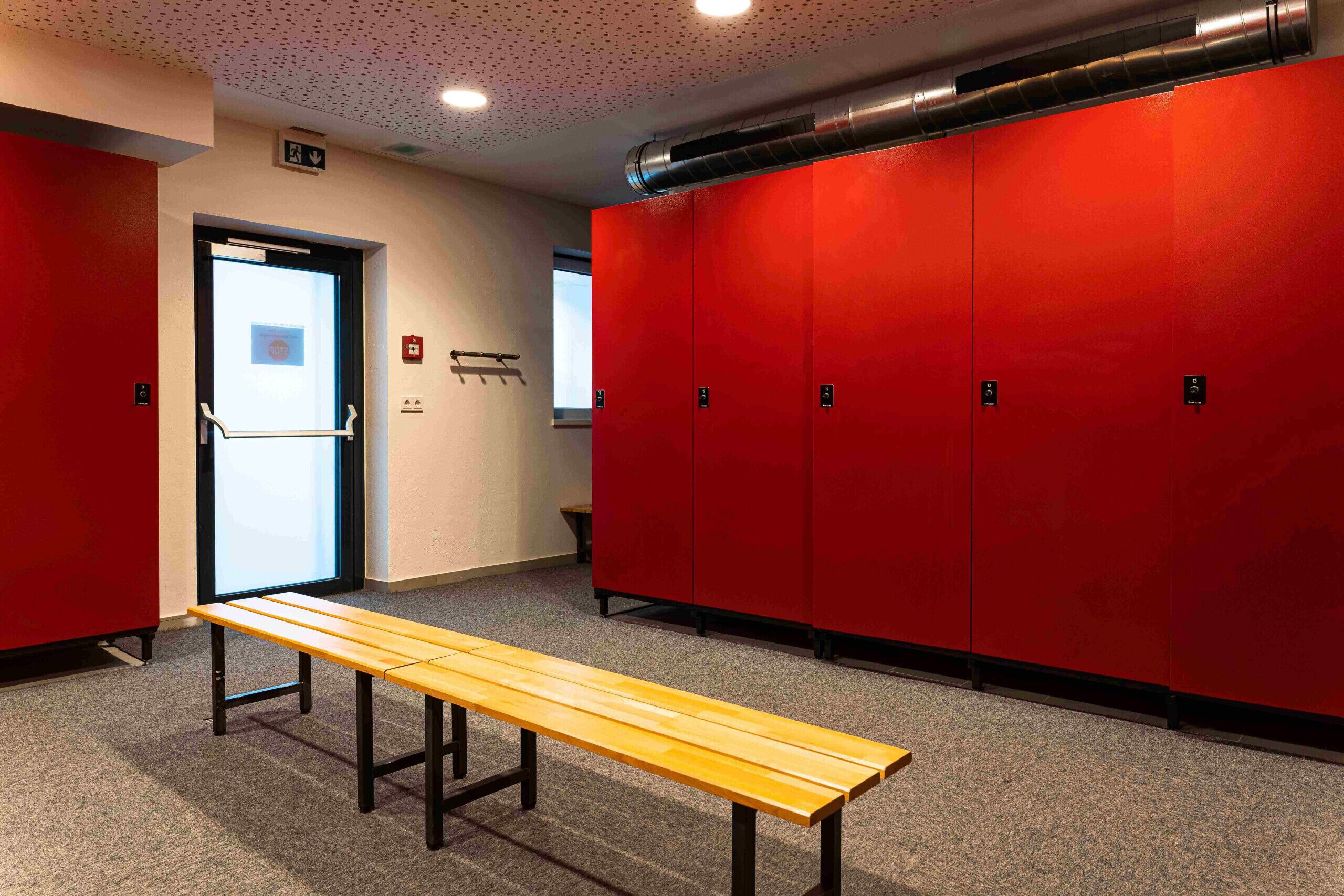 A locker room with red lockers, a bench, and a door with a frosted glass panel.