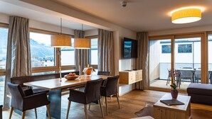 A modern hotel room with a dining area, a sofa, a TV, and a balcony with a view.