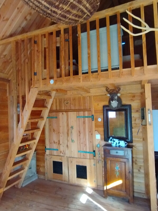 Ein Holzblockhaus-Innenraum mit einer Holztreppe, einem kleinen Holzschrank mit Spiegel und einem dekorativen Tierkopf an der Wand.