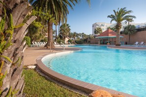 A swimming pool with lounge chairs and palm trees. - NEW Heated Pool & HOT Tub! Top-Floor-Ocean View! (Galveston)