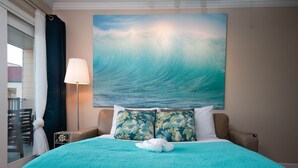 Et hotelværelse med en stor seng, udsigt til havet og et maleri af en bølge.