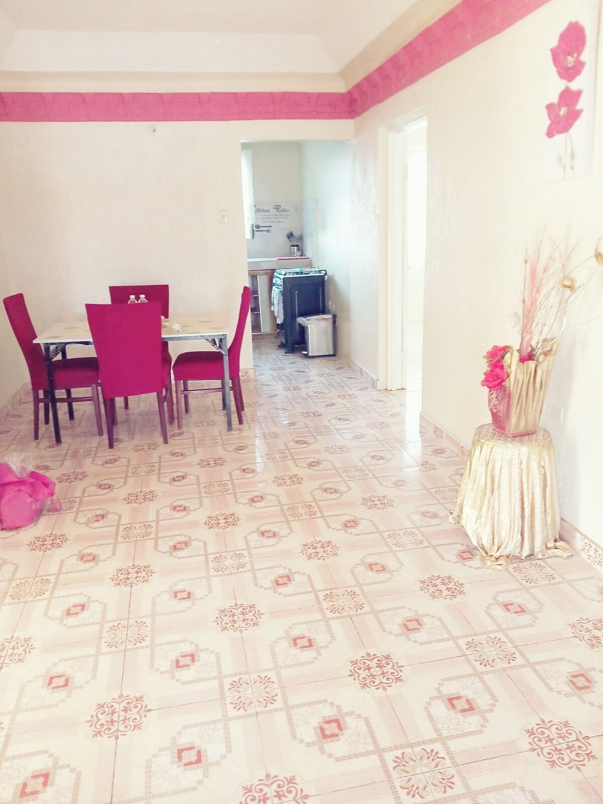 Zona pranzo con tavolo e sedie, cucina sullo sfondo e un vaso decorativo sul pavimento.