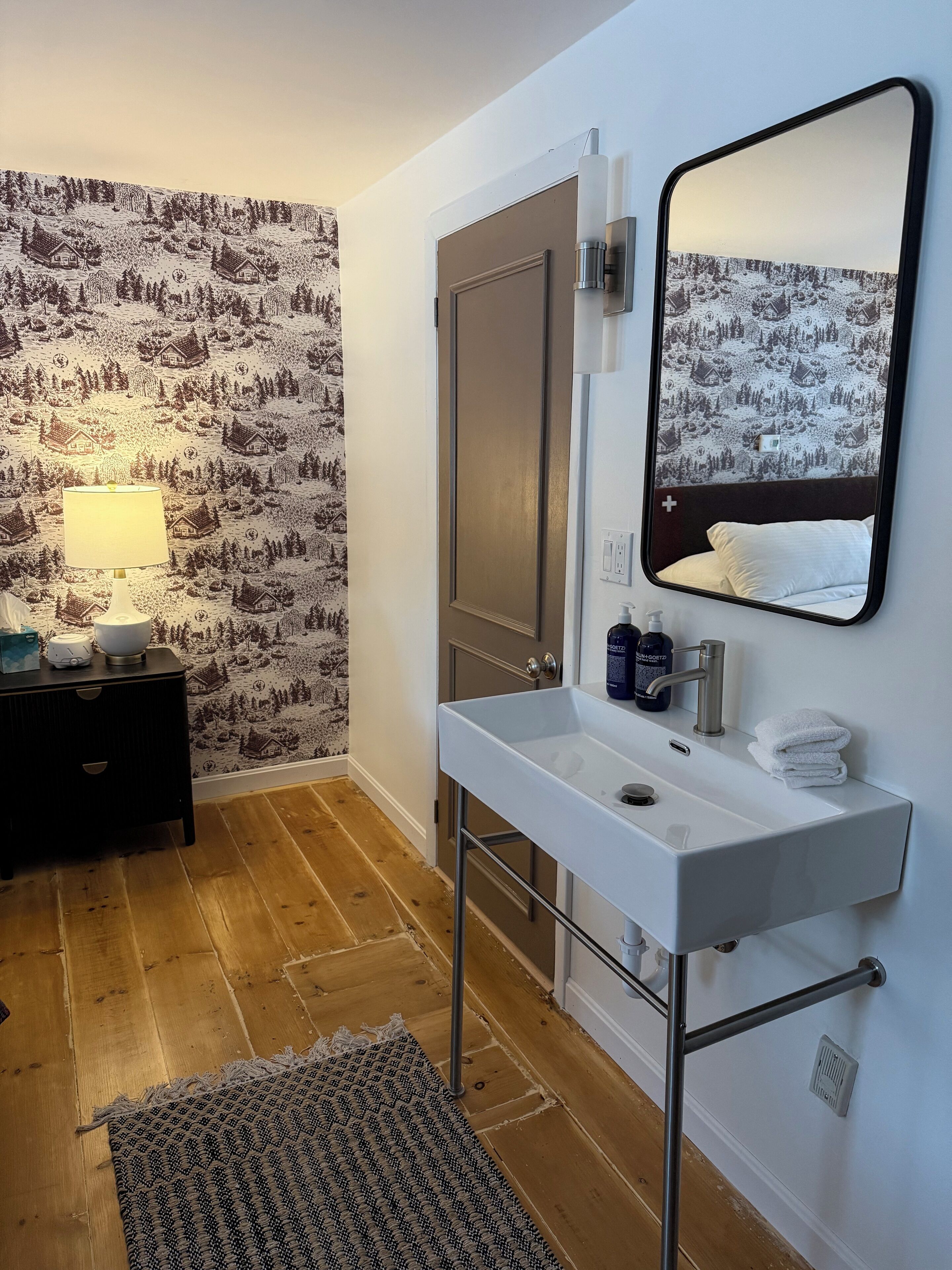 A modern bathroom with a white sink, mirror, and a decorative wallpaper depicting a snowy landscape.