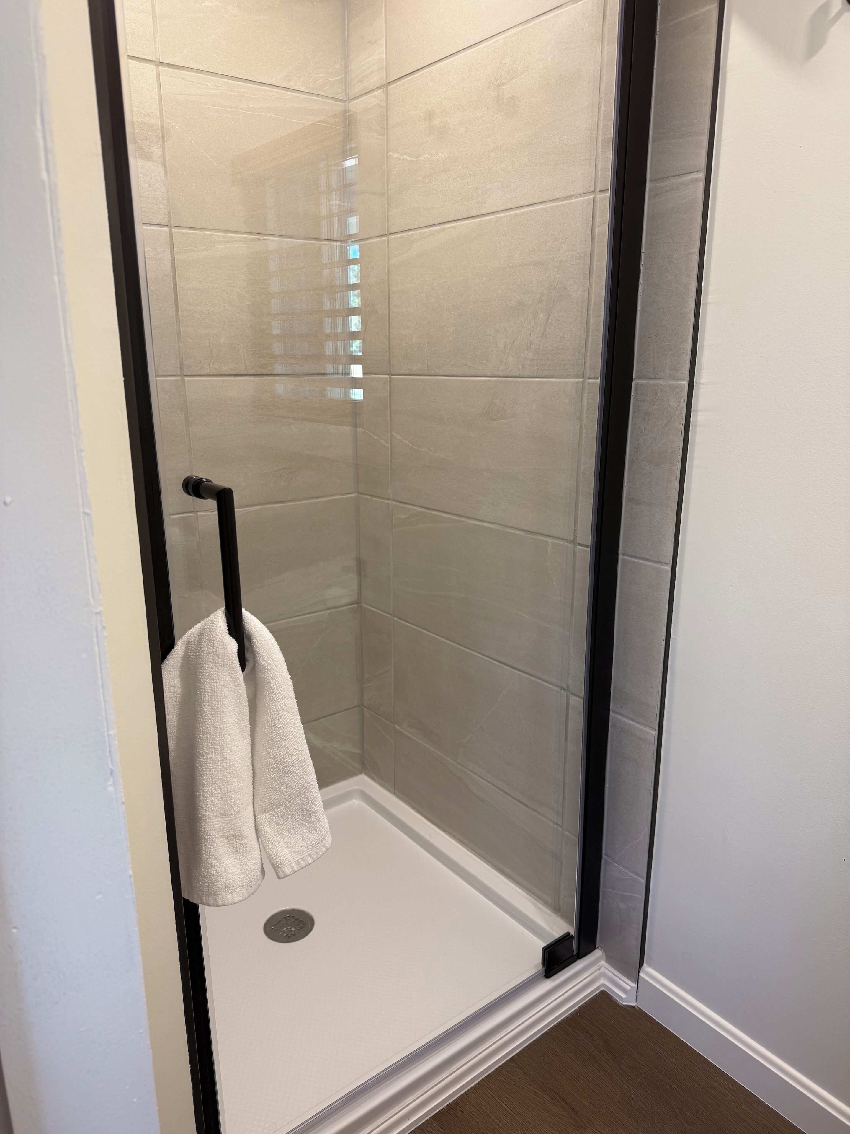 Un espacio de ducha con puerta de cristal, azulejos color beige y una toalla blanca colgada en un perchero.