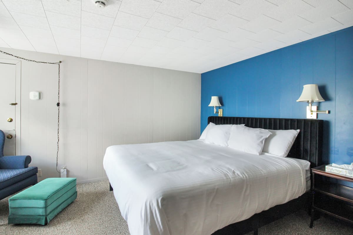 A hotel room with a large bed, a blue accent wall, a white door, and a small blue chair.