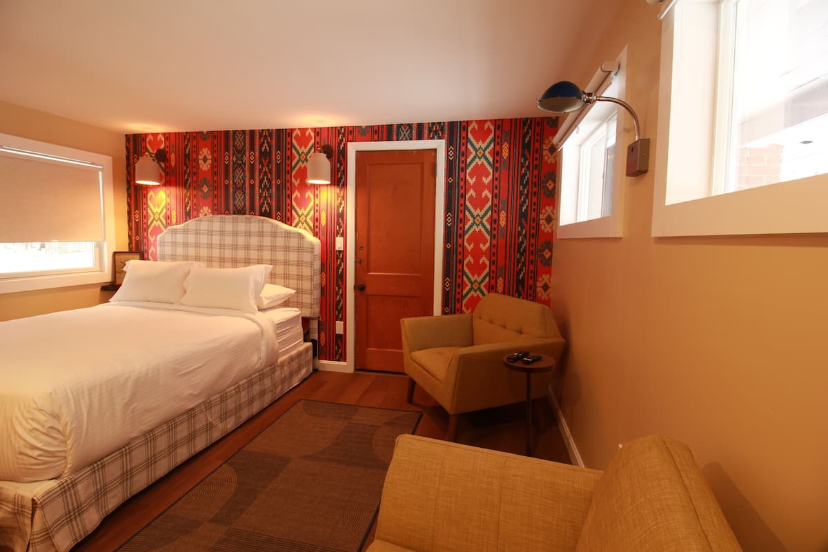 A hotel room with a bed, a chair, a small table, and a door.
