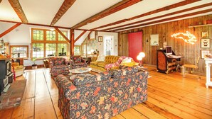 A spacious living room with wooden beams, a patterned sofa, a yellow armchair, and a red door. - COHO Inn & Motor Lodge (Weston)
