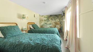 Habitación con dos camas, cada una con colcha verde, una mesita de noche con lámpara y un mural de un árbol en la pared.