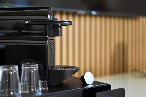 Une machine à café dotée d’un écran numérique, d’un réservoir d’eau et de plusieurs verres transparents, le tout posé sur une surface noire.