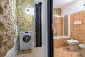 Une petite salle de bain équipée d’un lave-linge, d’une baignoire et de toilettes.