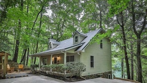Ein zweistöckiges Haus mit Veranda, umgeben von dichtem Wald.