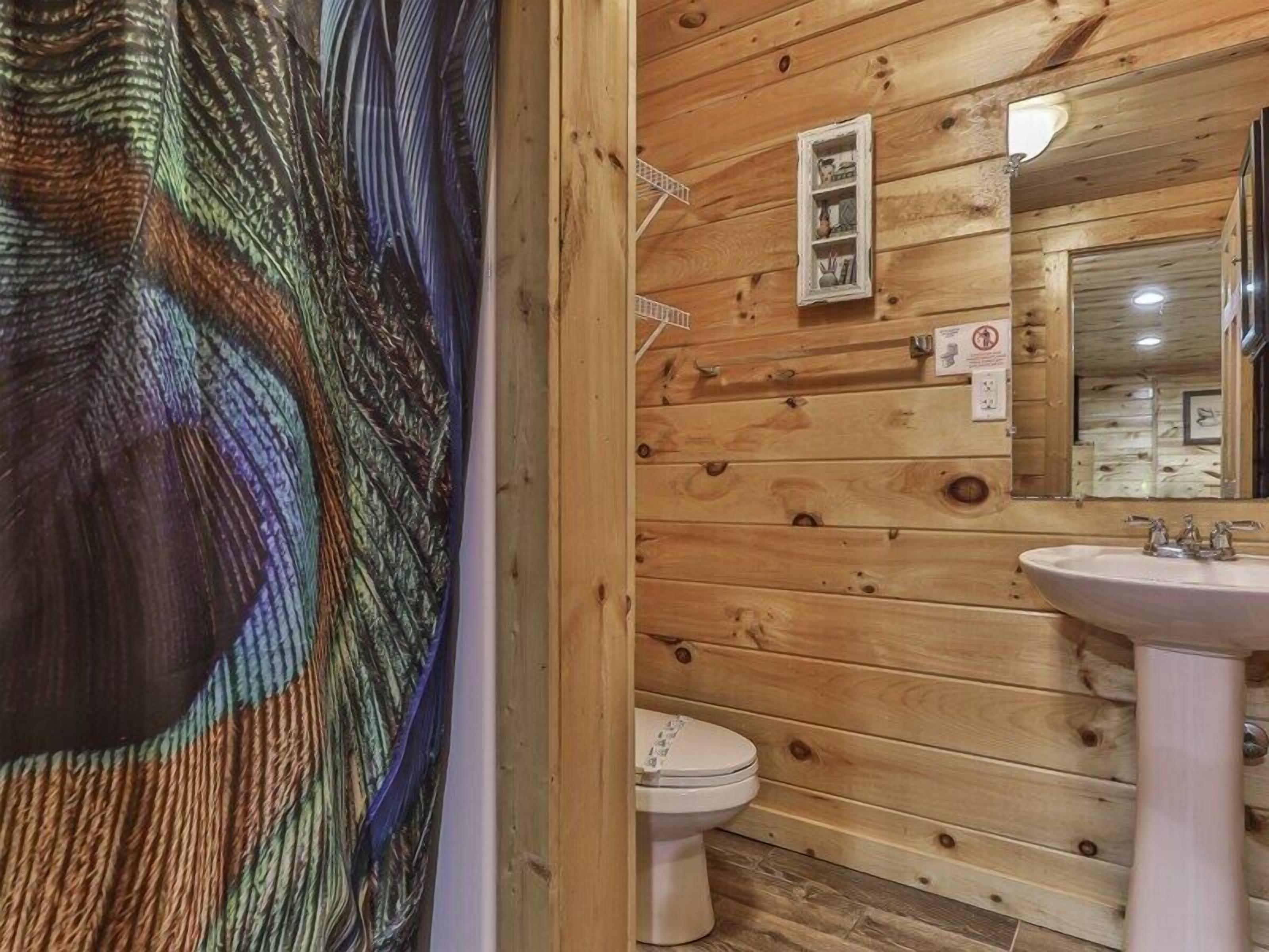 A wooden cabin bathroom with a white sink, a toilet, and a mirror.