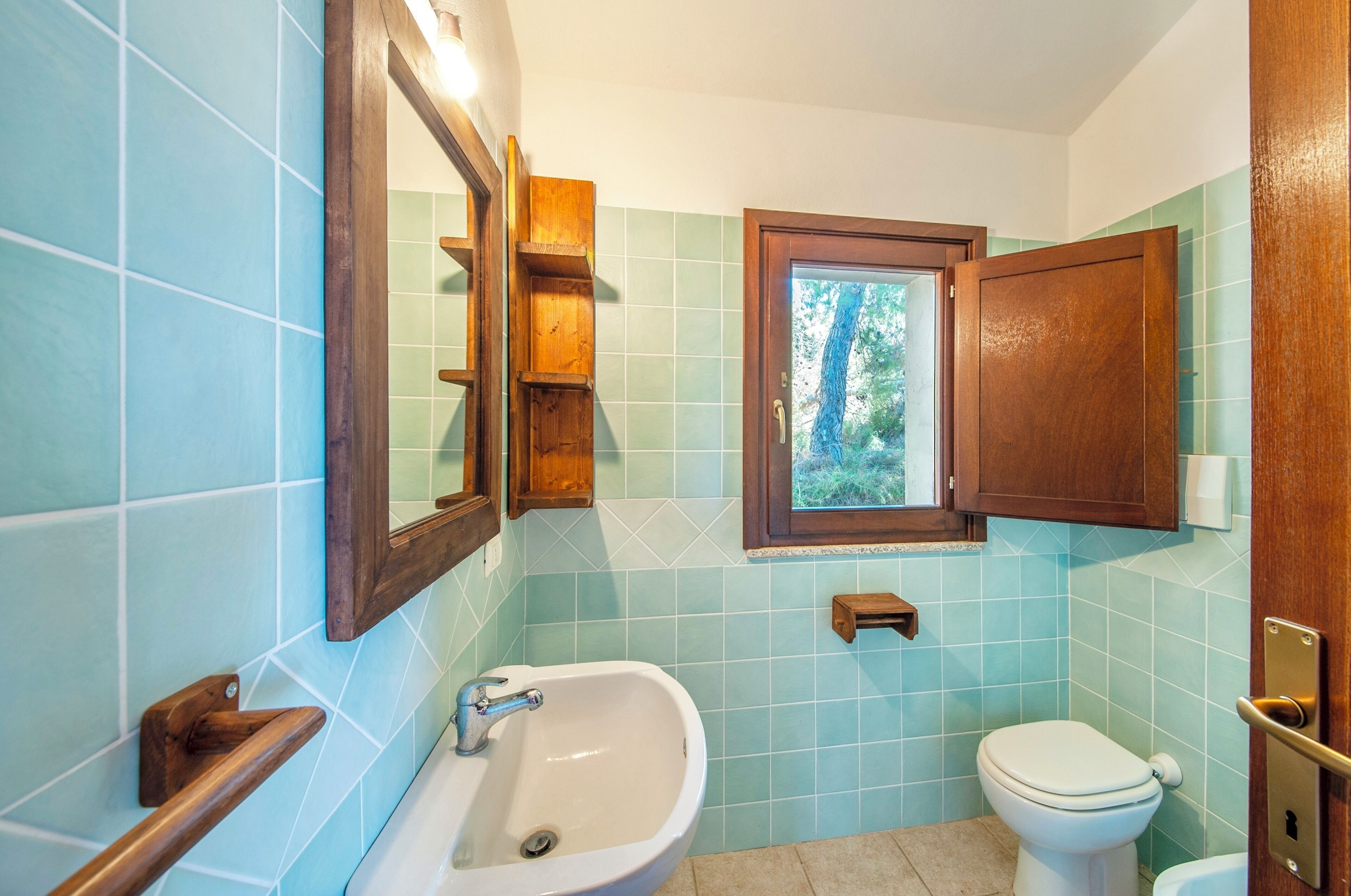 A bathroom with a sink, toilet, and a window with a view of greenery.