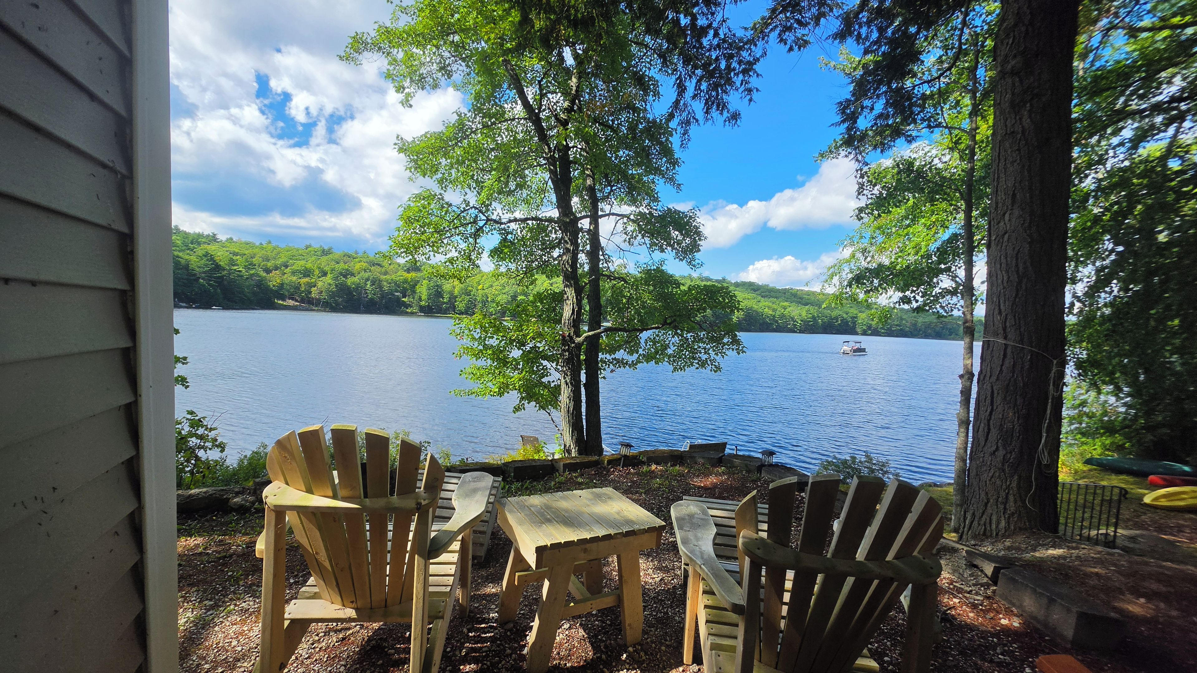 Une vue sur le lac depuis une véranda équipée de chaises Adirondack et d’une table, donnant sur un lac paisible et des collines boisées.