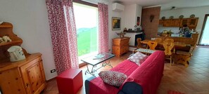 Een gezellige woonkamer met een rode bank, een houten kast en een eethoek met een tafel en stoelen.
