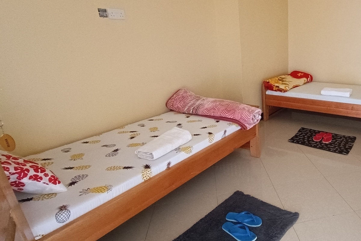 A small, clean room with two single beds, a small table, and a chair.