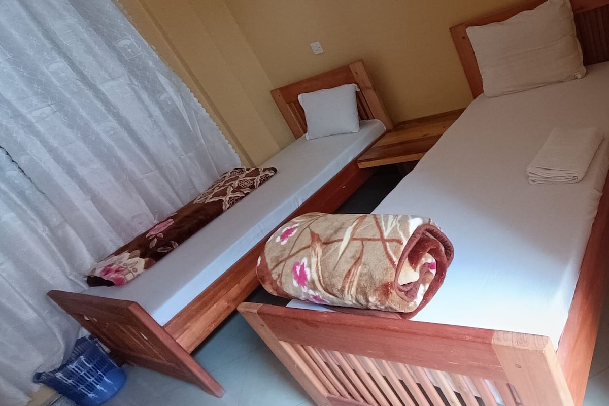 A single-bed room with a wooden headboard, a wooden bench, and a small table.