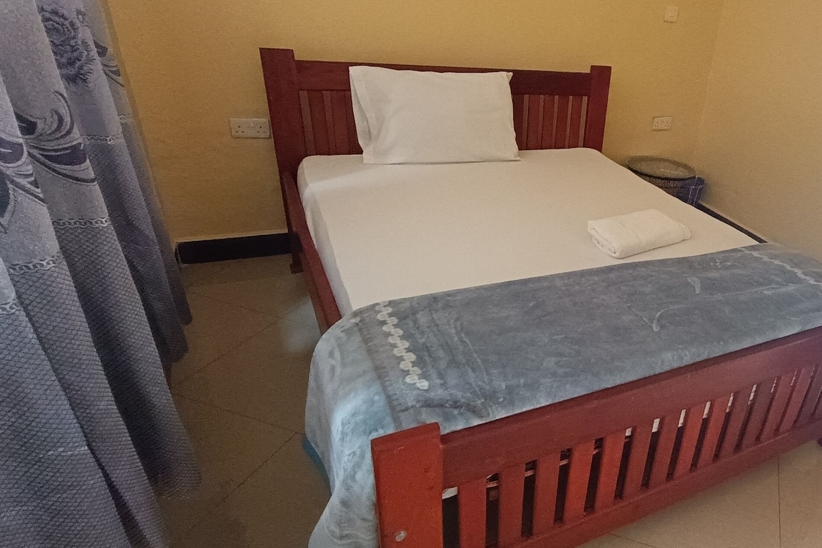 A bed with a white mattress and a grey blanket, a wooden headboard, and a white pillow.