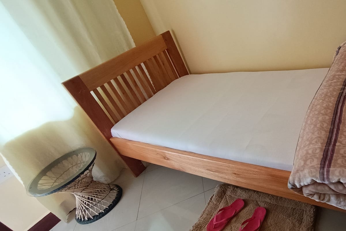 A single bed with a wooden frame, a white mattress, and a patterned blanket.