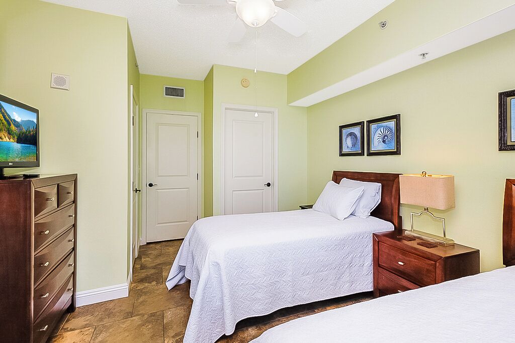 A bedroom with two beds, a TV, a dresser, and artwork on the wall.