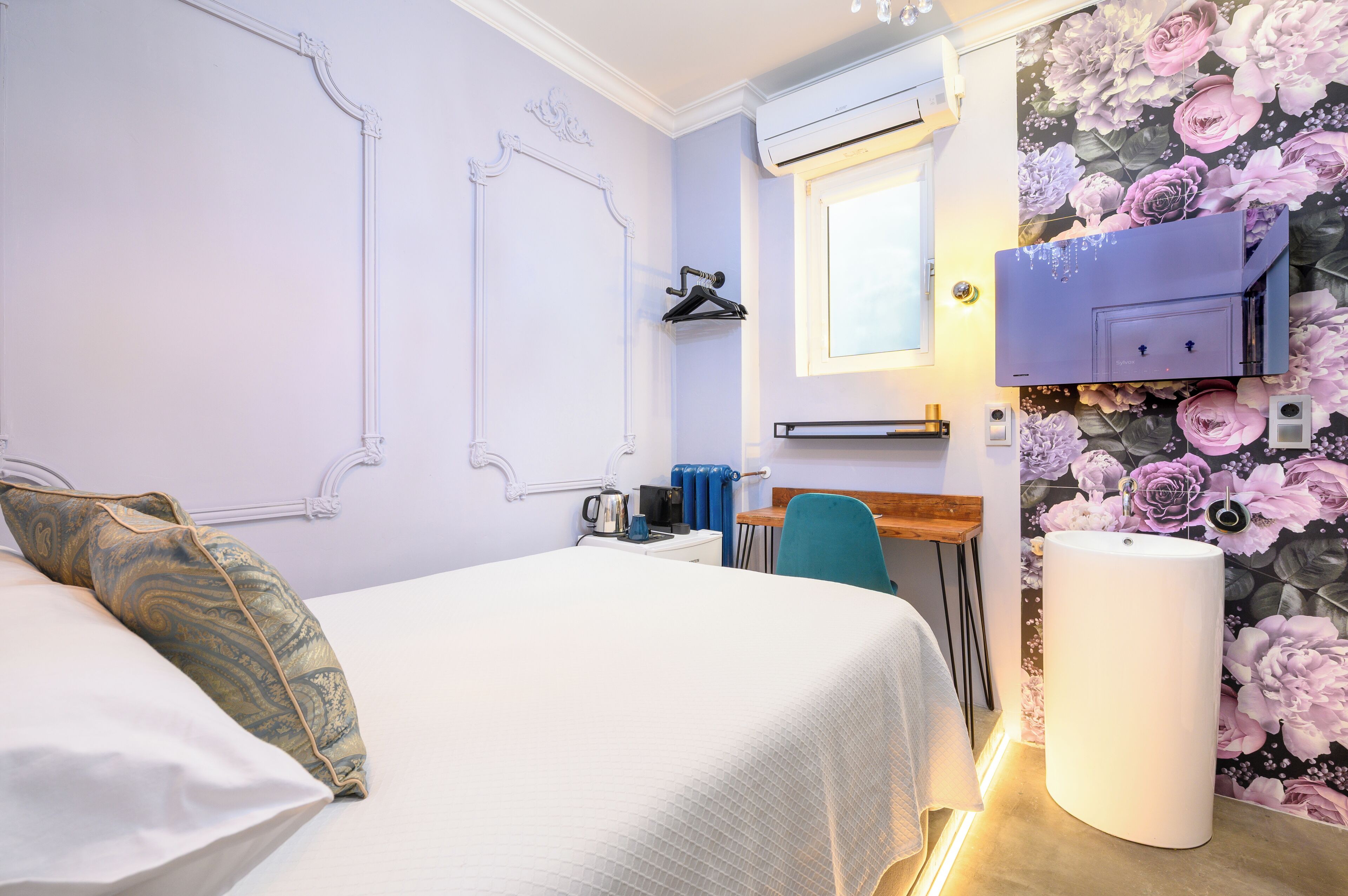 Een slaapkamer met een bed, een bureau, een stoel, een radiator en een aan de muur bevestigde televisie.