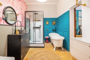 Un baño con cabina de ducha de vidrio, una bañera blanca, tocador con espejo y una puerta color turquesa.