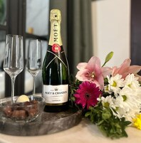 Una botella de champán Moët & Chandon, dos copas y un arreglo floral sobre una mesa.
