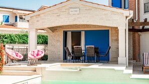 A villa with a stone facade, a blue door, and a pool area with lounge chairs.
