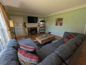 A living room with a sofa, ottoman, and a fireplace. - Brick House on the River at Riverside Point Resort (Park Rapids)