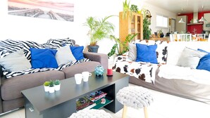 Una sala de estar moderna con un sofá, una mesa de centro y un reposapiés. Se ven plantas y una estantería al fondo.